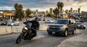 Motorcyclist in full protective gear avoiding distracted SUV driver at busy Oakland intersection during rush hour.
